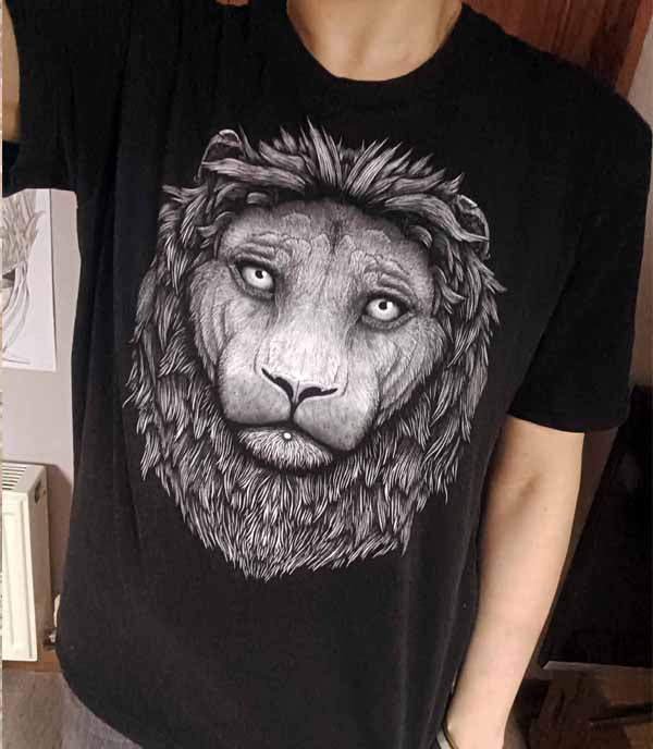 A person wearing a black short-sleeve T-shirt with a large grayscale lion face graphic printed on the front, shown in a real indoor setting.