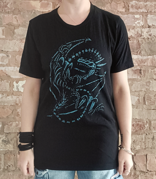 Person wearing a black t-shirt with a blue bone dragon graphic design against a brick wall.